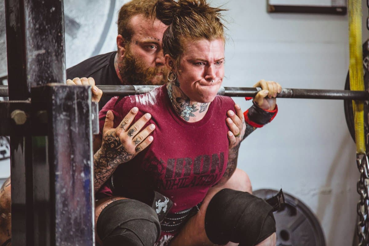 A coach spots his client through a heavy barbell back squat