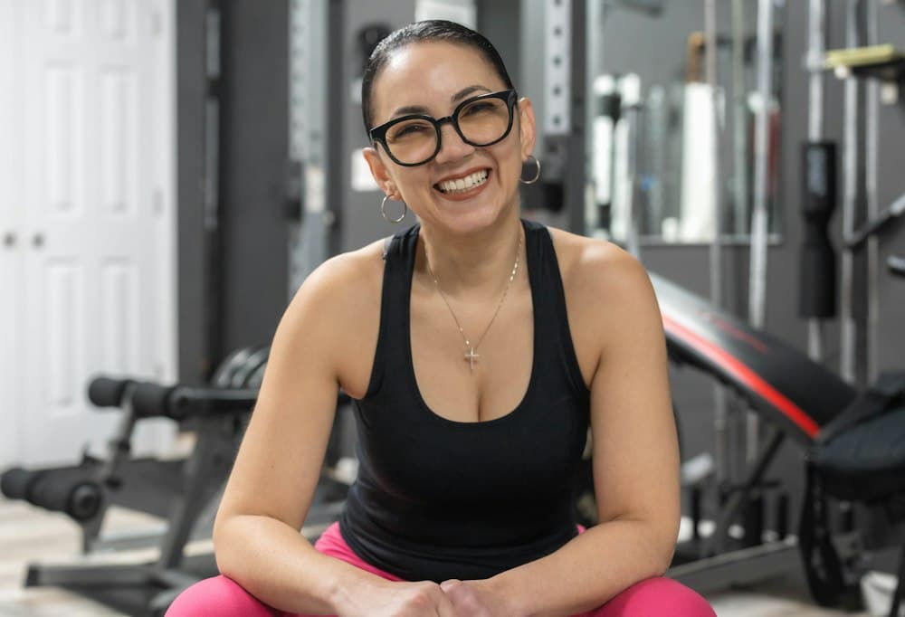 Portrait of a smiling female coach with glasses, sitting in a home gym